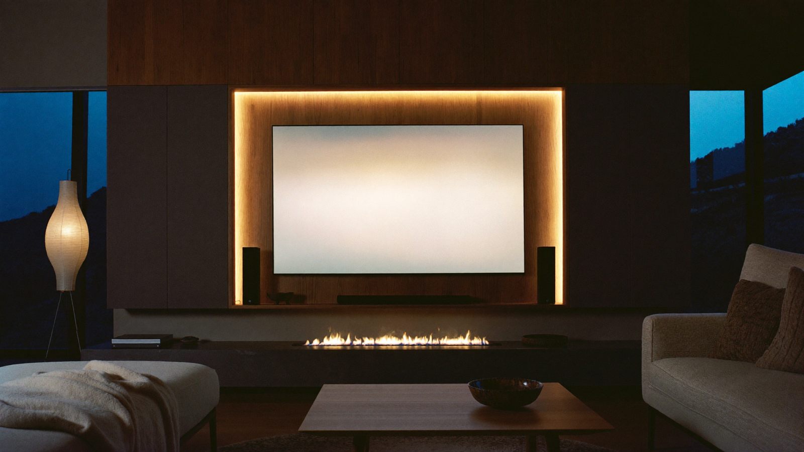 A modern lounge at night with a wall-mounted screen and a soft halo of light glowing behind it